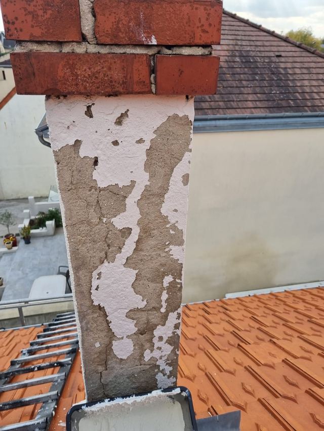 Souche de cheminée à l'enduit écaillé et fissuré, au-dessus d'une toiture en tuiles, secteur de Mitry-Mory