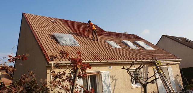 Application d'un revêtement coloré sur une toiture en tuiles mécaniques, fenêtres de toit protégées par des bâches, secteur de Mitry-Mory